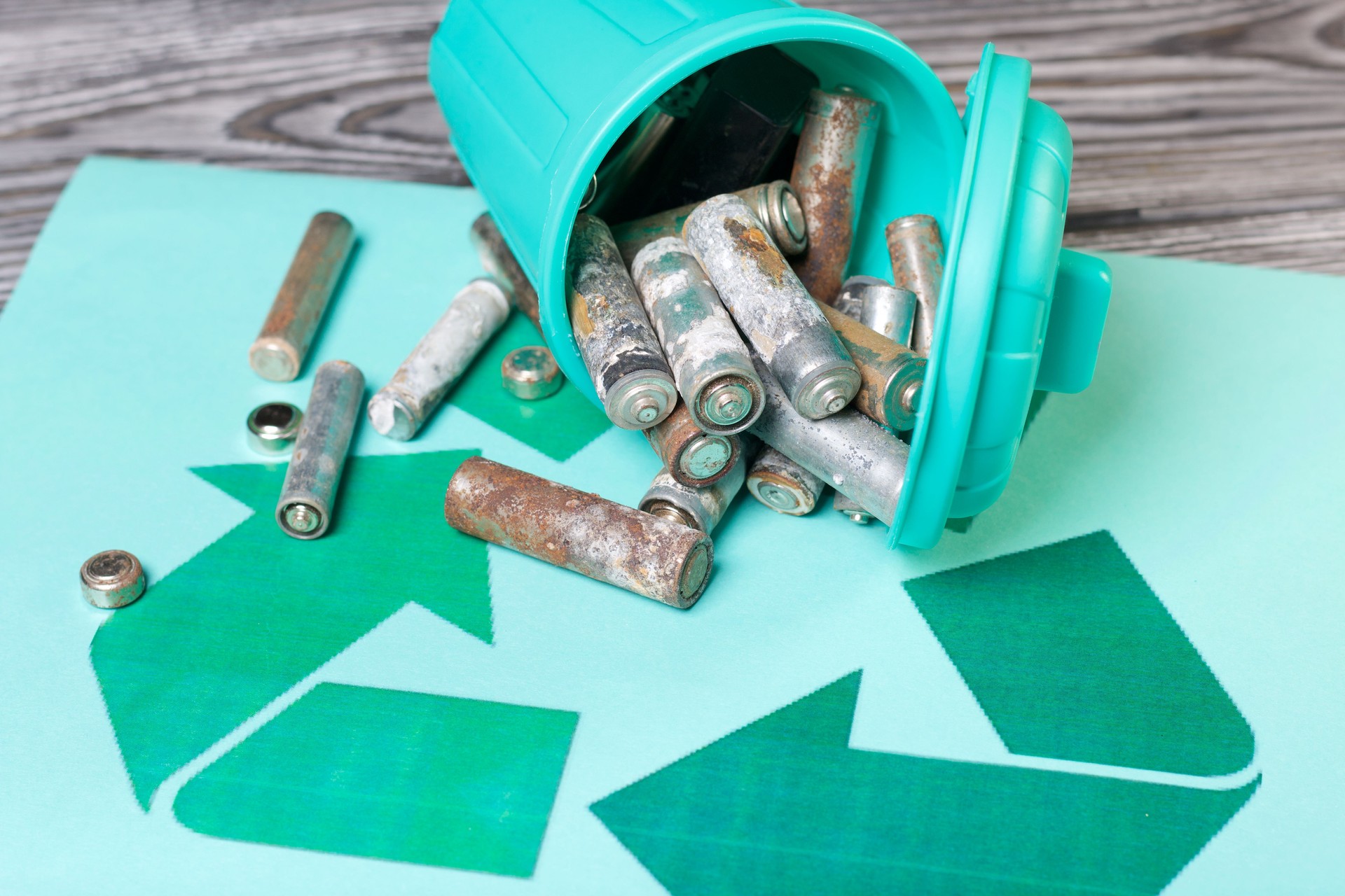 Papierkorb mit Deckel, gekentert auf der Seite. Tank gefüllt mit Altbatterien. Die Batterien sind mit Korrosion bedeckt. Abfallrecycling-Symbol. Tag der Umwelt.